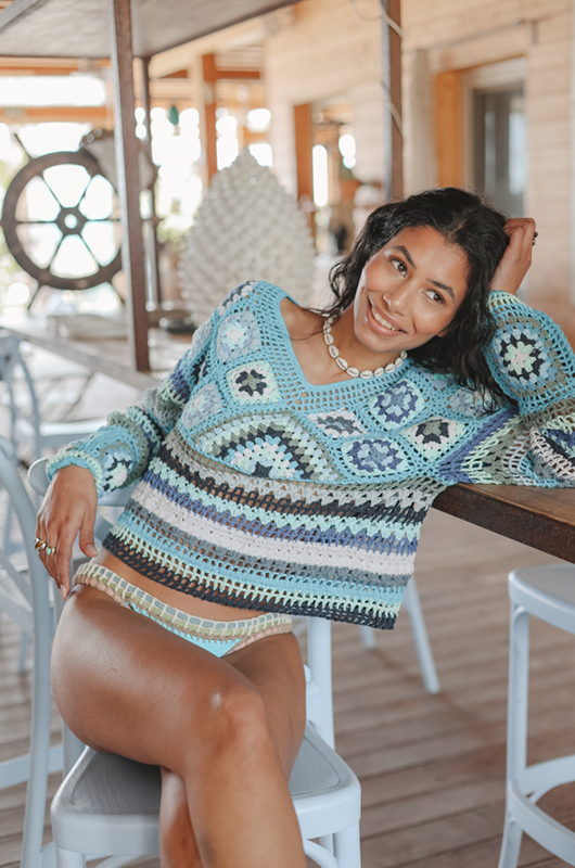 Front view of a model wearing granny‑square crochet sweater with geometric motifs in textured open-knit