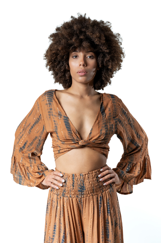 A close-up of the front of the outfit, focusing on the knotted top design, smocked waistband, and textured fabric with metallic accents.