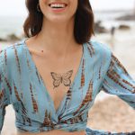 Close-up of a smiling model on the beach wearing a sky blue and rust tie-dye lurex set with a knotted top and wide-leg pants.