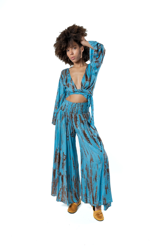 Studio image: A model wearing the sky blue and rust tie-dye lurex set, knotted top and wide-leg pants.