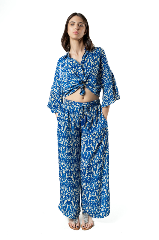 Woman posing in a blue and white printed co-ord set with a tied shirt and wide-leg palazzo pants, hands in pockets, studio background.