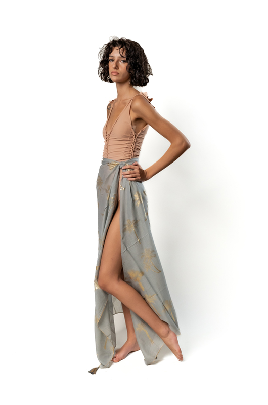 Model wearing long grey pareo with golden palm print tied at the waist.