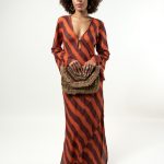 Beige clutch with black and gold geometric pattern, held behind the back