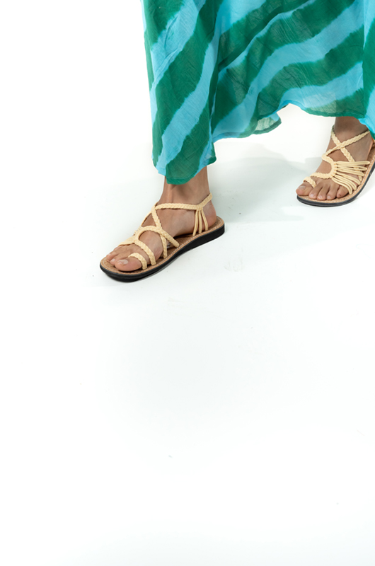Close-up of beige rope flat sandals paired with a flowy green and blue striped summer dress.