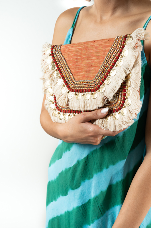 Detailed view of a bohemian clutch with fringes, beads, and golden embellishments, styled with a striped maxi dress.
