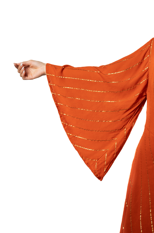 Close-up of a wide bell sleeve in rust-orange fabric with golden stripes, arm extended sideways.