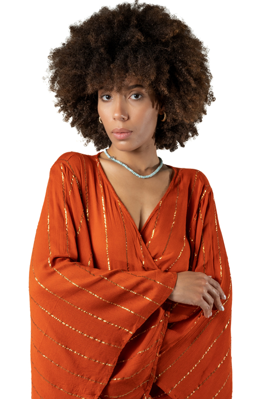 Close-up of a woman in a rust-orange dress with golden stripes, showing the V-neckline and wide bell sleeves.