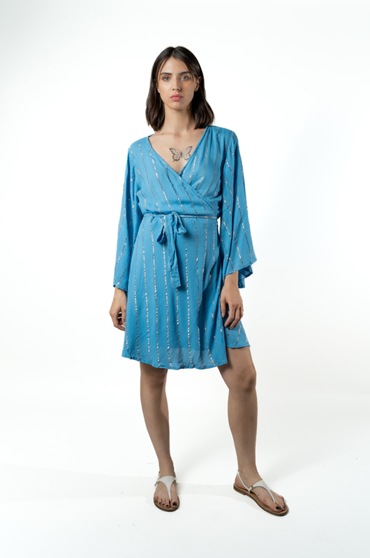 A woman wearing a sky-blue wrap dress with silver stripes, tied at the waist, standing front view with arms relaxed.