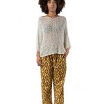Woman wearing a loose white open-knit sweater with mustard geometric patterned trousers and brown friulane shoes