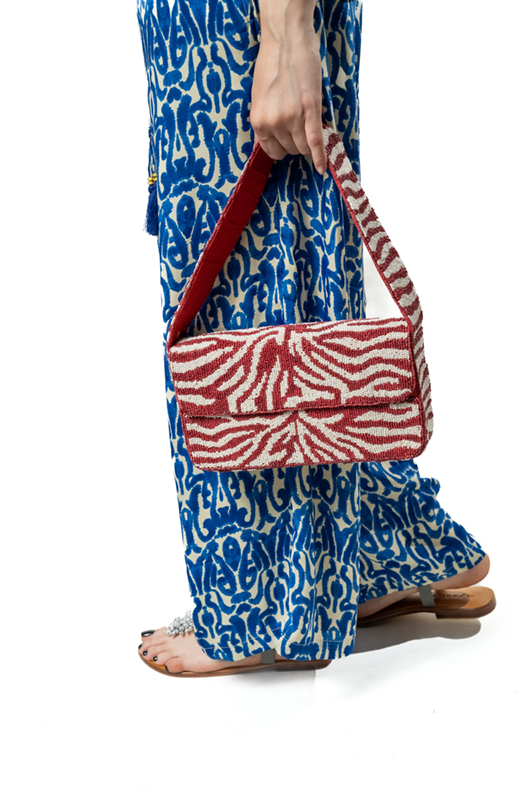 Close-up of a red and white patterned handbag held by a woman, showing details of the bag and the blue and white printed pants.