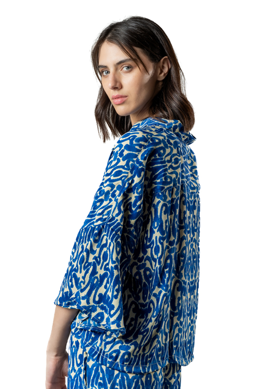 Close-up side view of a woman wearing a blue and white printed co-ord set, looking back at the camera, studio background.