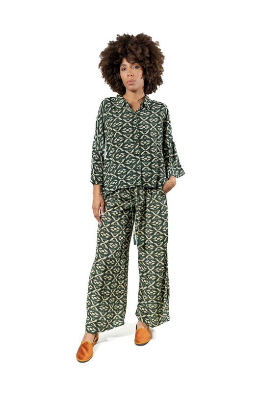 A model wearing a dark green printed co-ord set with a loose-fit shirt and matching wide-leg pants, standing facing forward with hands in pockets.