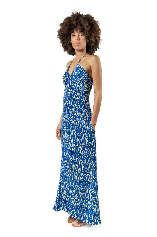 Side view of a woman in a flowing blue and white halterneck maxi dress with a bold abstract pattern, showing the dress’s silhouette and fit.
