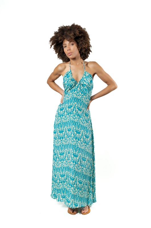 Model in a turquoise halter maxi dress with white pattern, posing confidently with one hand on her hip in a studio setting.