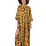 Model wearing a mustard yellow and white geometric printed long dress with 3/4 sleeves and a braided brown belt, styled with green shoes.