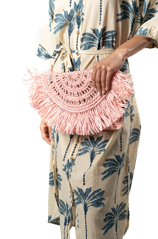Close-up of a pink fringed woven clutch held by the model wearing the beige dress with blue palm tree print.