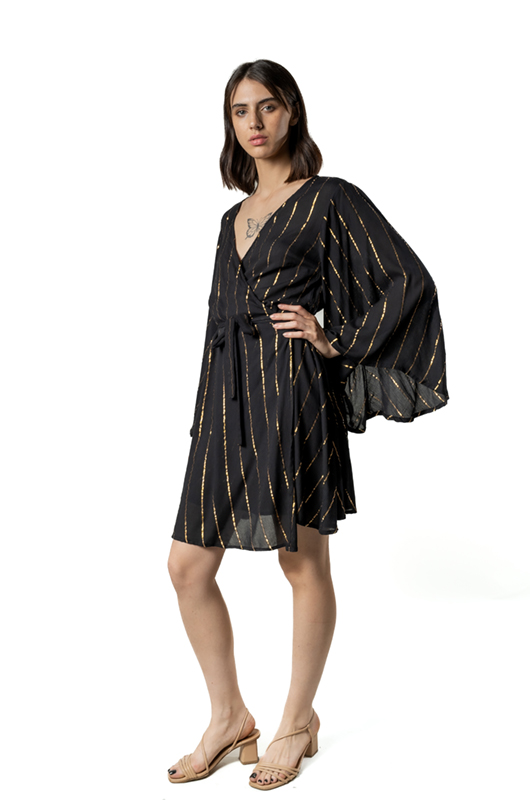 A model in a black wrap dress with golden diagonal stripes, posing sideways with one hand on her hip.
