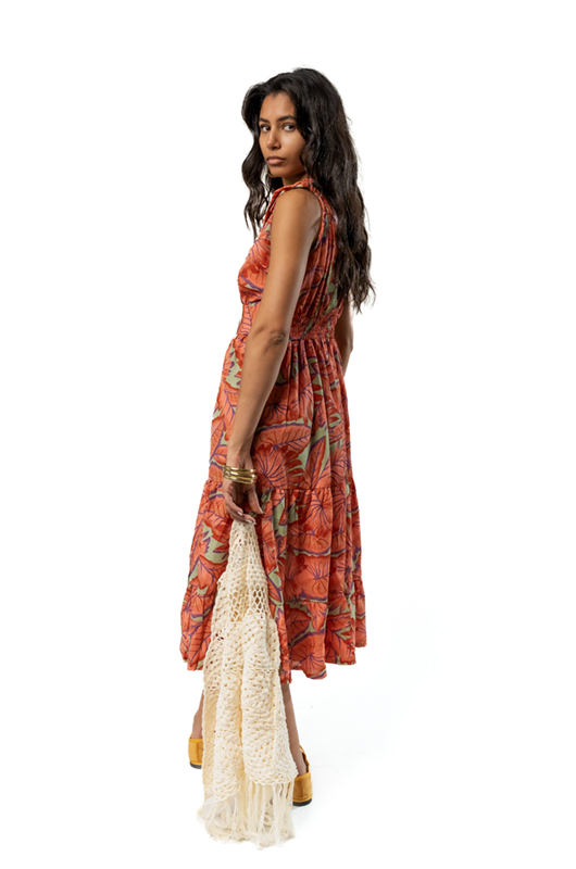 Back view of a woman in an orange floral print midi dress, holding a cream crochet vest in one hand.