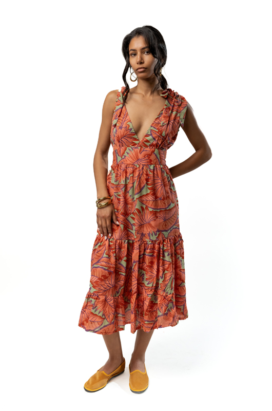 A woman posing in an orange tropical floral midi dress with a plunging neckline and tiered skirt.