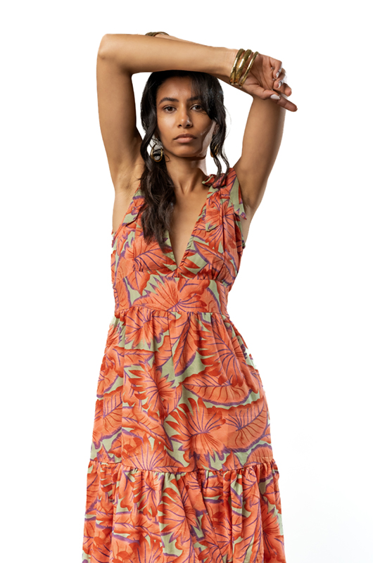 Close-up of a woman in an orange floral print dress, raising her arms to highlight the plunging neckline and bold tropical pattern.