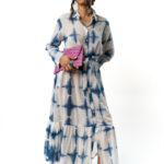 Woman wearing a long-sleeved button-down midi dress with blue tie-dye patterns, styled with a pink clutch and pink flats.