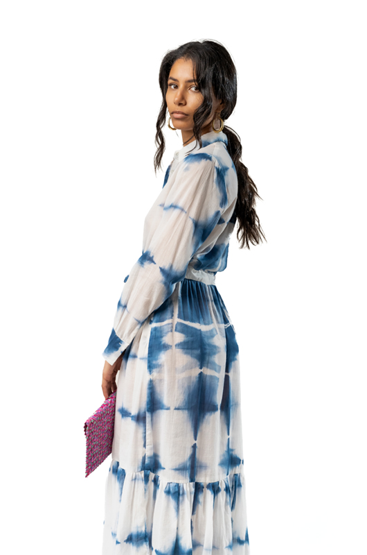 Side profile of a woman in a blue tie-dye midi dress, holding a pink clutch.