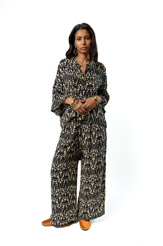 A woman posing in a studio wearing a printed loose shirt and matching wide-leg pants.