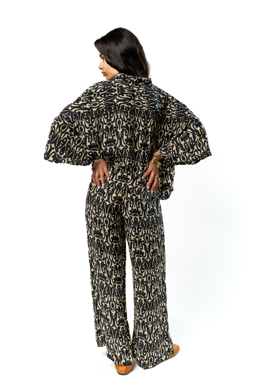 A back view of a woman wearing a patterned loose shirt and wide-leg pants, posing with hands on hips.