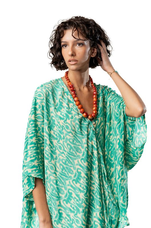 Close-up of a model wearing a light green patterned kaftan-style top and an orange bead necklace.