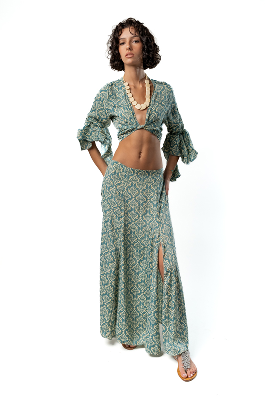 A woman wears a green patterned blouse with a deep V-neckline and tied front, featuring voluminous ruffled sleeves.