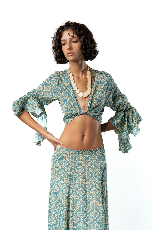 Close-up of the green patterned blouse with deep neckline and ruffled sleeves, accessorized with a chunky white necklace.