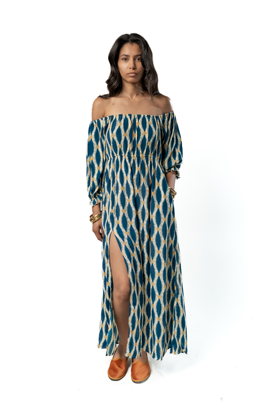Woman wearing a long blue off-shoulder dress with white and gold geometric print, side slit and 3/4 sleeves