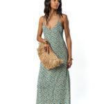 A model wearing a green patterned maxi dress, accessorized with a straw clutch bag.