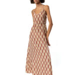 A model wearing a long, sleeveless maxi dress with thin straps, featuring a brown and cream geometric pattern, photographed from a three-quarter angle.