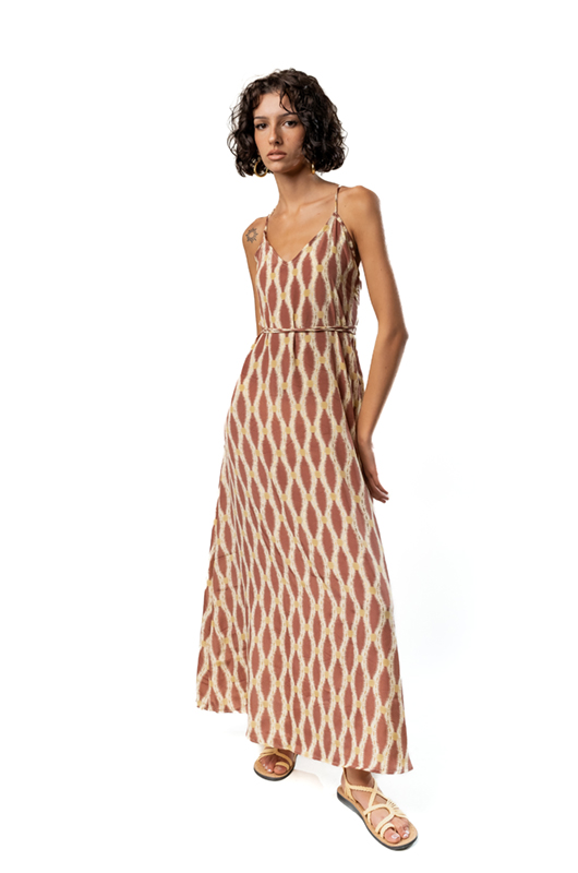 A model wearing a long, sleeveless maxi dress with thin straps, featuring a brown and cream geometric pattern, photographed from a three-quarter angle.