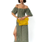 Woman wearing a long green off-shoulder dress with ethnic print, side slit and yellow woven clutch bag