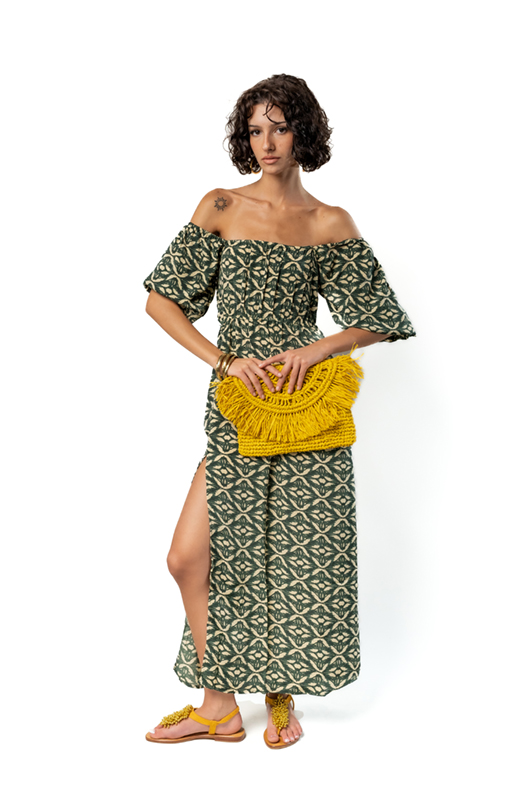 Woman wearing a long green off-shoulder dress with ethnic print, side slit and yellow woven clutch bag