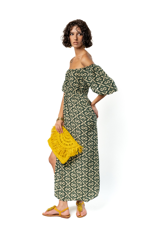 Side view of long green off-shoulder ethnic print dress styled with a yellow clutch