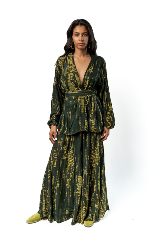 "Front view of a woman wearing a dark green two-piece set with a gold abstract print, featuring a deep V-neck wrap kimono-style top with a belt and a long matching skirt."