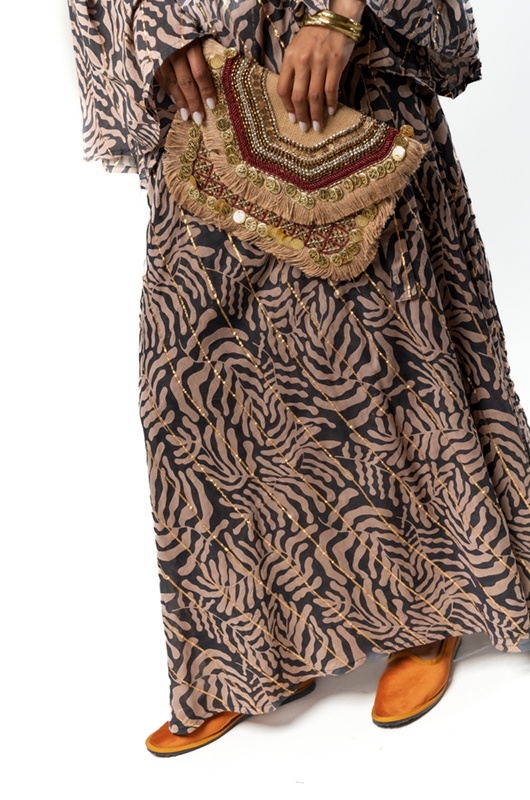 Close-up of a decorative boho clutch with beads and tassels, paired with a beige and black leaf print maxi dress.
