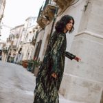 Woman walking barefoot on a cobblestone street wearing a green tie-dye lurex maxi kaftan dress.