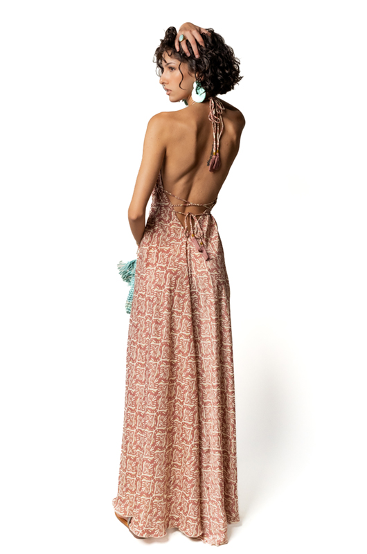 "Back view of a woman wearing an open-back halter maxi dress with a pink and beige leaf print, tying details at the back."