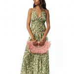 Model wearing a sleeveless green halter-neck maxi dress with abstract print, paired with multiple bangles and holding a pink fringed woven clutch.