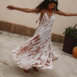 Woman twirling outdoors in a white and brown tie-dye maxi dress, creating movement in the fabric of the dress.