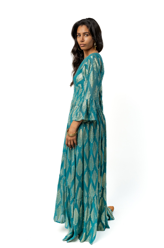 "Model in a teal and gold bohemian dress with V-neck and flared sleeves, shown from the side to display the flowy silhouette."