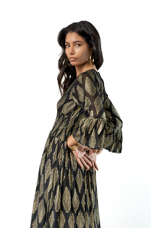 Close-up three-quarter view of a black maxi dress with gold geometric leaf patterns, highlighting the sleeves and fitted waist.