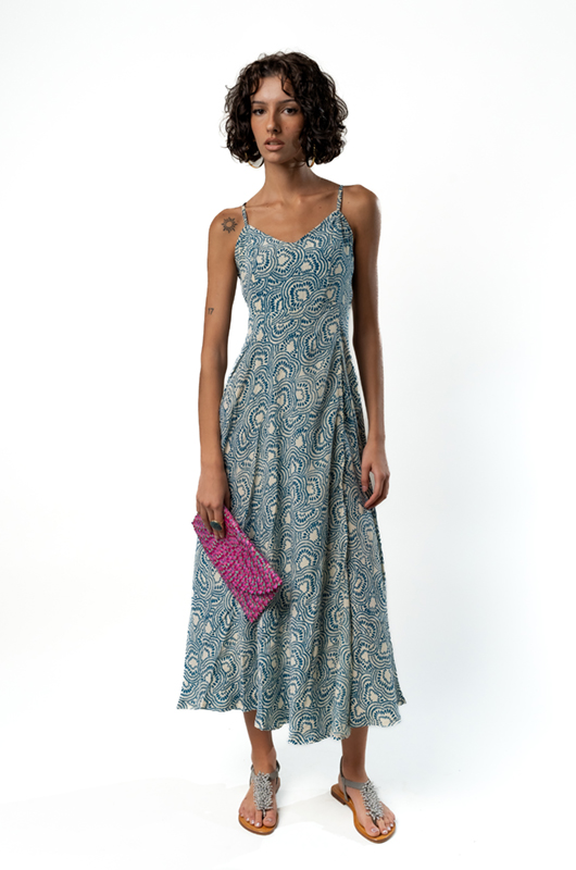 Front view of a sleeveless midi dress with thin straps, in a blue and cream paisley pattern, paired with a small pink clutch.