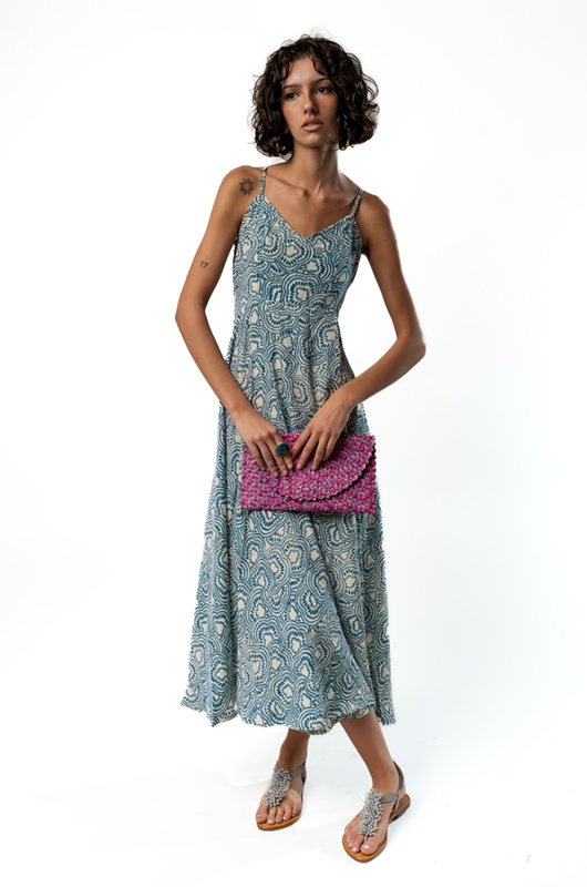 Angled front view of a blue and cream paisley sleeveless midi dress, accessorized with a pink clutch.