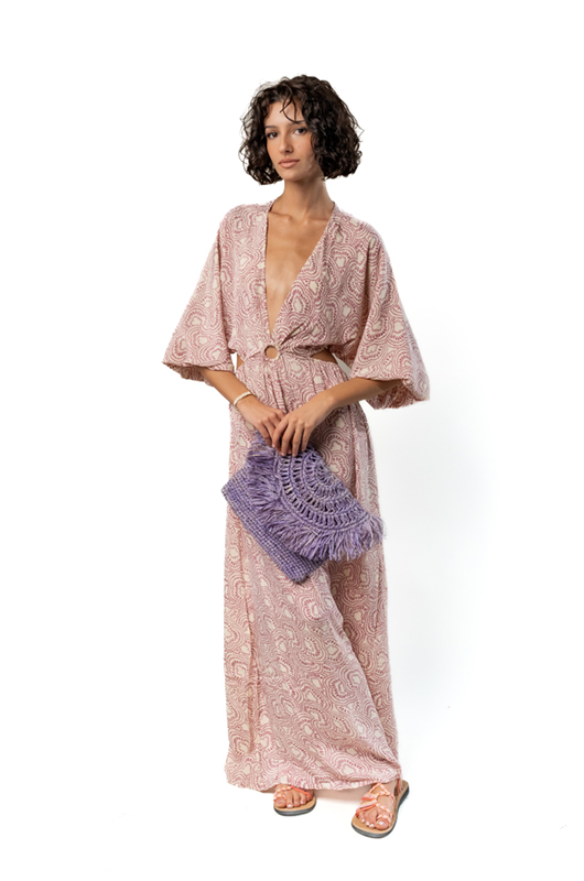 Studio front view of a woman in a one-shoulder beige maxi dress with blue palm print, paired with tan flat shoes.