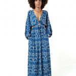 Alt text: Front view of a woman wearing a long-sleeved, deep V-neck blue ikat print maxi dress with a ring detail at the waist and side cutouts.